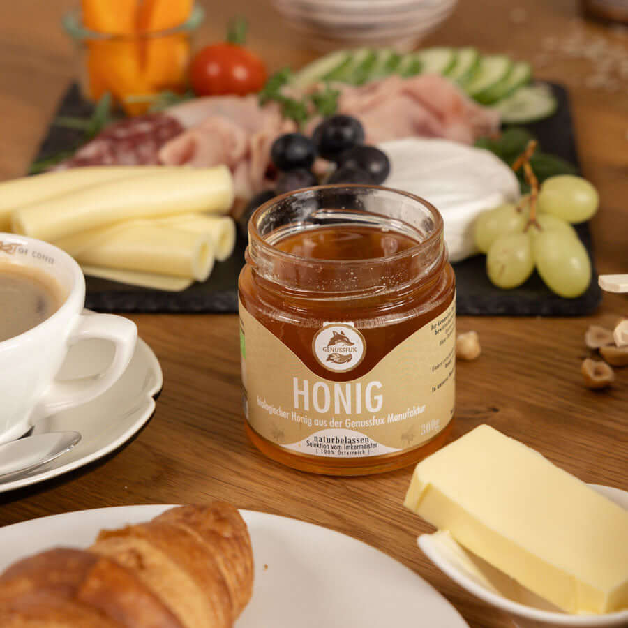 Brunch-Flatlay auf Holztisch mit Genussfux Bio-Honig aus Österreich, naturbelassen, umgeben von Croissant, Käse und Kaffee