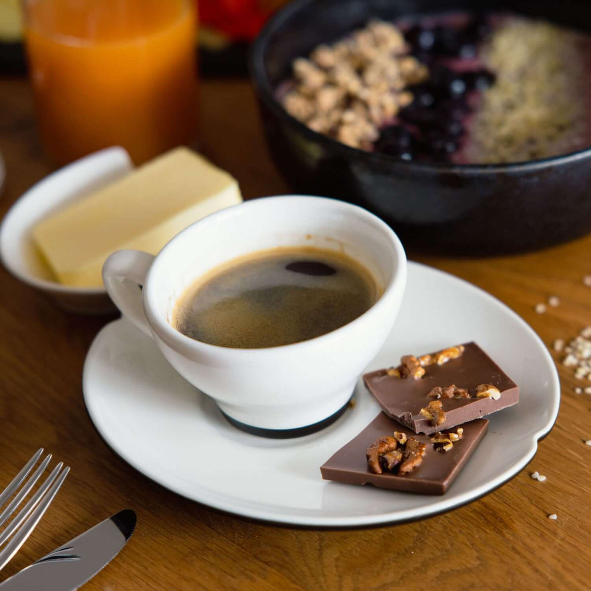 Frühstücks-Flatlay mit Tasse Kaffee, Croissant und Stücken handgeschöpfter Bio-Walnuss-Honig-Schokolade mit karamellisierten Walnüssen auf Holztisch