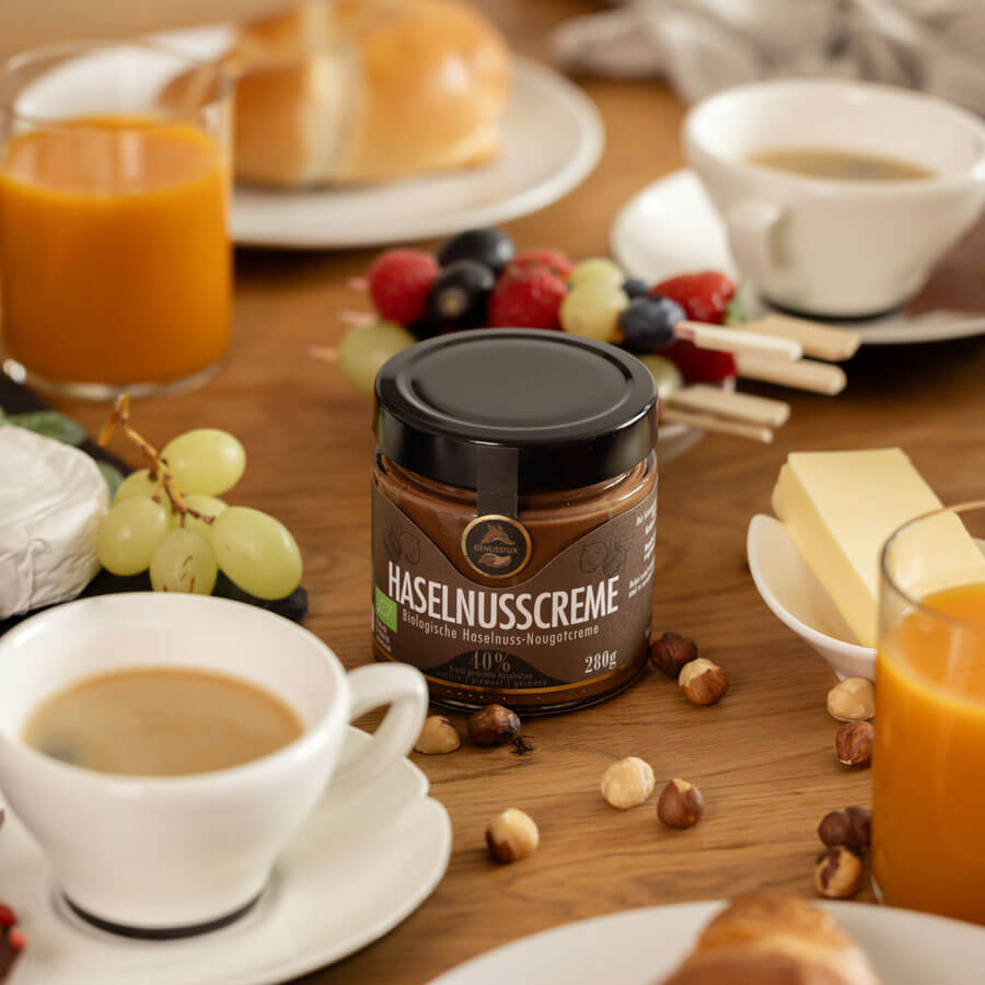 Brunch-Flatlay mit Genussfux Bio-Haselnusscreme (40 % Haselnüsse) aus Österreich, palmölfrei, mit Kaffee, Orangensaft und Croissant