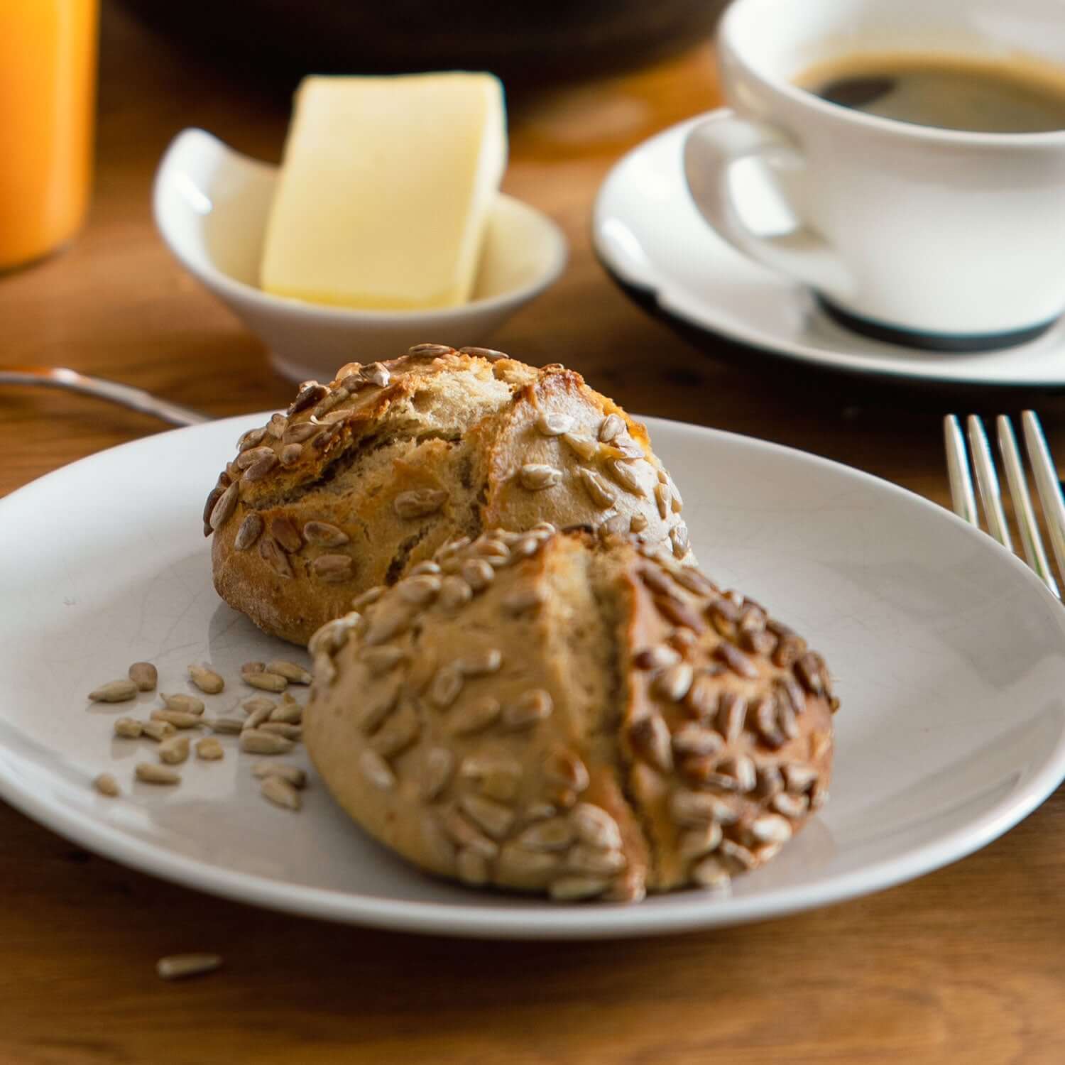 Frisch gebackene Brötchen im Brunch-Flatlay, bestreut mit Genussfux Bio-Sonnenblumenkernen aus eigenem Anbau auf Holztisch