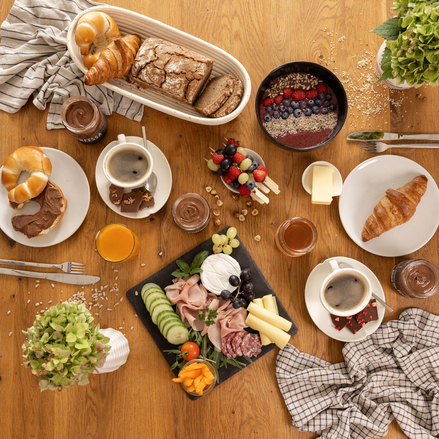 Brunch-Tafel auf Holztisch mit Genussfux Haselnusscreme (40 % Haselnüsse), Bio-Honig aus eigener Imkerei, Nougatcreme, Gebäck, Käse, Obstspießen und Kaffee