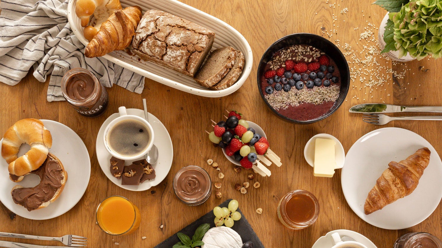 Brunch-Tafel auf Holztisch mit Genussfux Haselnusscreme (40 % Haselnüsse), Bio-Honig aus eigener Imkerei, Nougatcreme, Gebäck, Käse, Obstspießen und Kaffee