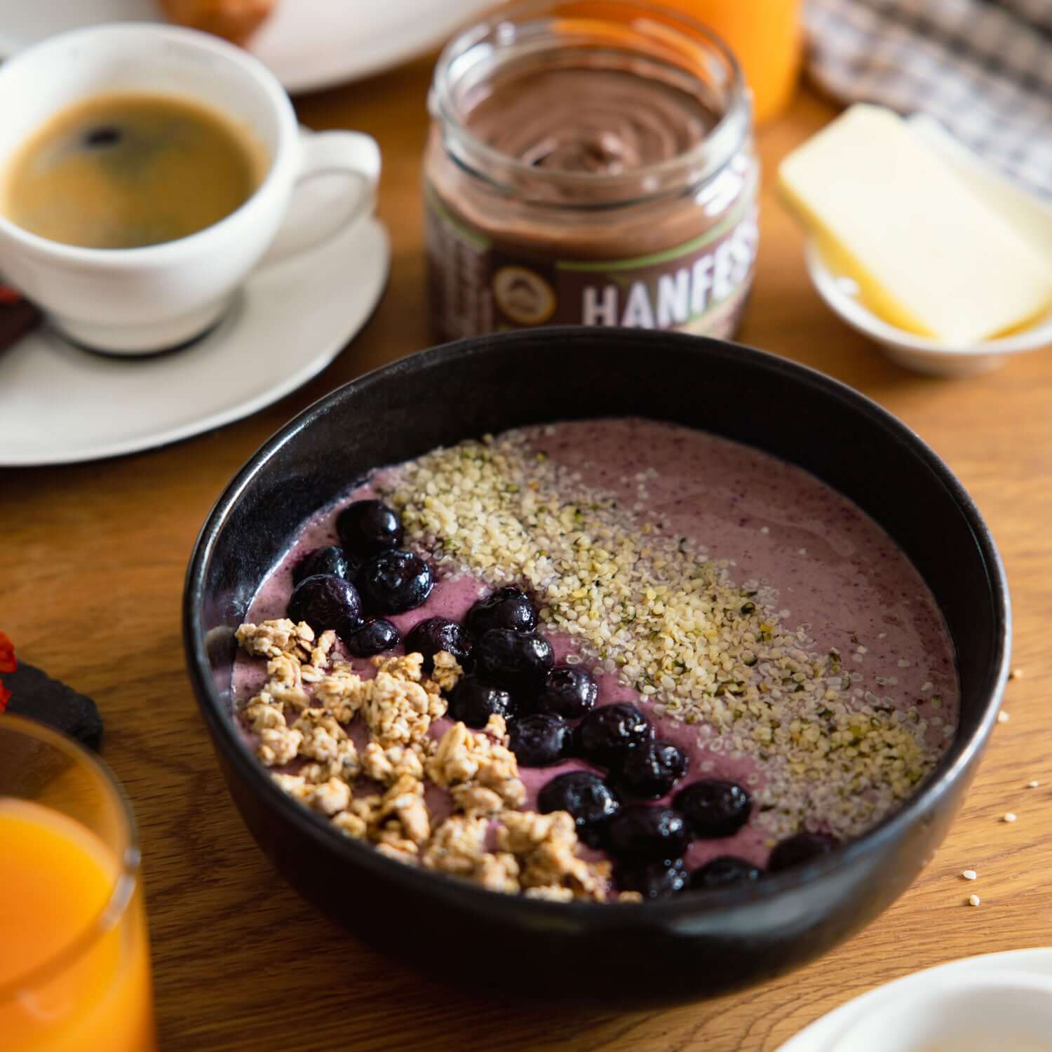 Gesunde Smoothie-Bowl mit Genussfux Bio-Hanfsamen (geschält), frischen Blaubeeren und Crunch-Müsli im Flatlay auf Holztisch