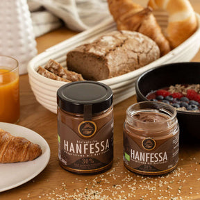 Brunch-Flatlay mit zwei Gläsern Genussfux Hanfessa Nougatcreme (30 % geröstete Hanfsamen, palmölfrei, bio) auf Holztisch mit Brot und Smoothie