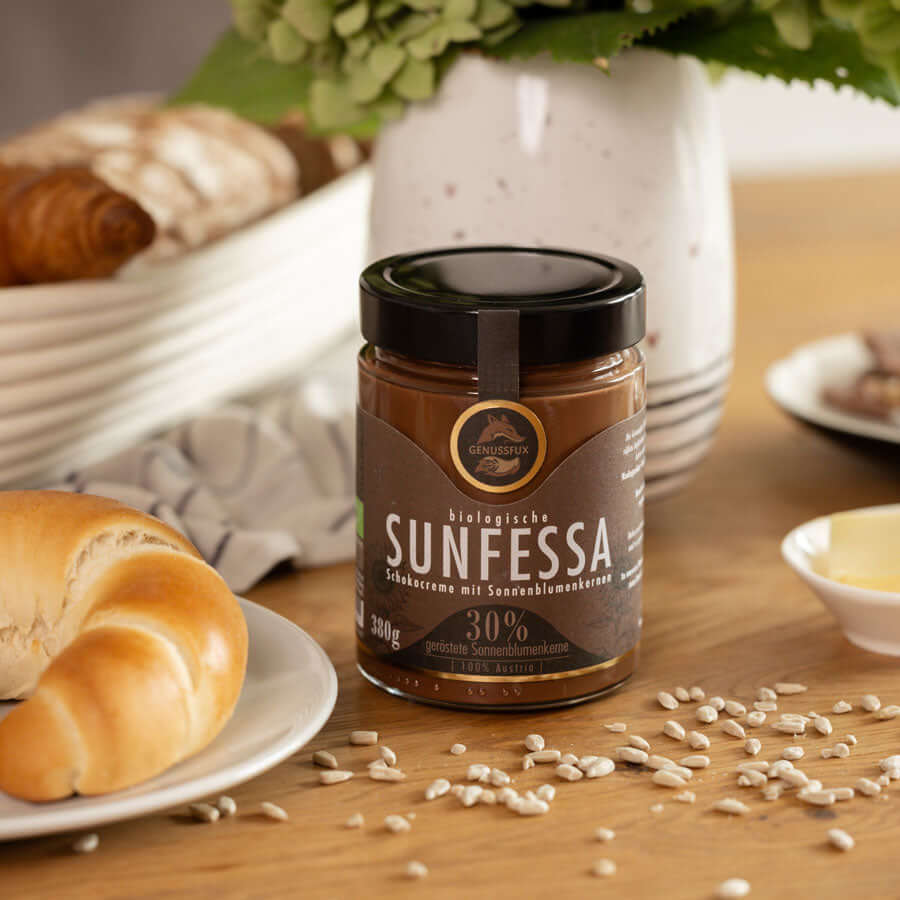 Brunch-Flatlay auf Holztisch mit Genussfux Sunfessa Schokoladencreme (30 % geröstete Bio-Sonnenblumenkerne), palmölfrei und handgemacht in Österreich, neben Croissant, Honig und Kaffee