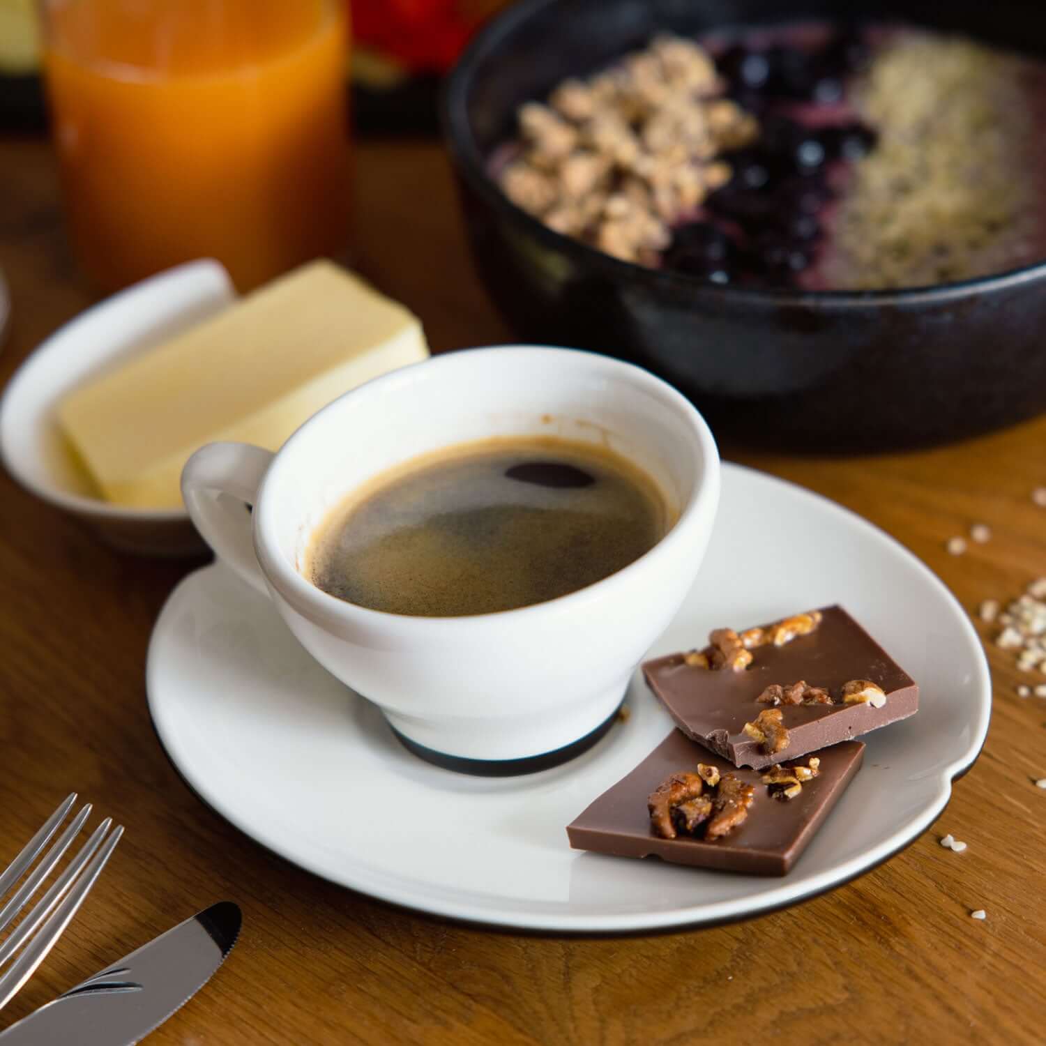 Frühstücks-Flatlay mit Tasse Kaffee, Croissant und Stücken handgeschöpfter Bio-Walnuss-Honig-Schokolade mit karamellisierten Walnüssen auf Holztisch